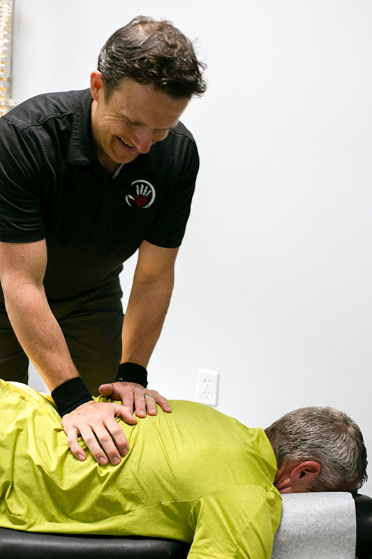 Chiropractor adjust low back of patient while they lay face down on massage table.